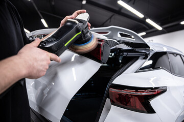 Detailing professional meticulously polishes a white cars paint and tail lamp, ensuring a...