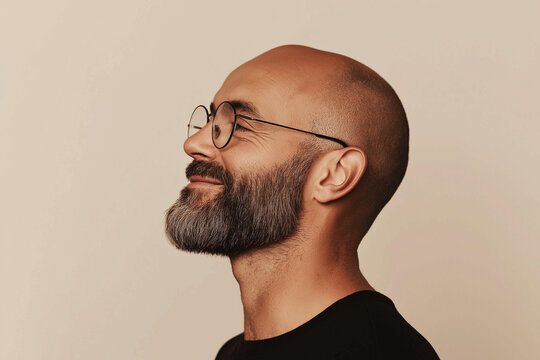 Studio portrait of smiling bald man wearing glasses, side profile view with neutral beige background