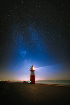 The Milky Way photographed at night with stars in the sky above a light beacon on the shor