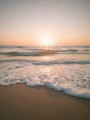 Gentle ocean waves washing over a sandy beach at sunset, with warm golden light reflecting on the water.