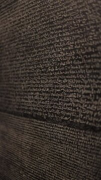 Vertical screen showing a detailed view of the Rosetta Stone, focusing on the inscriptions in ancient Egyptian hieroglyphs, which played a crucial role in decoding the ancient language.

