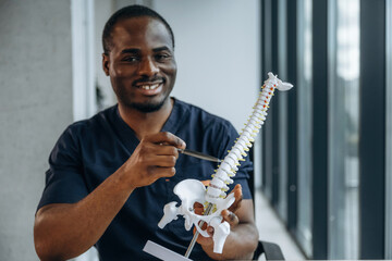 Pen in hand, showing the problematic on the spine model. Professional doctor is in his office indoors