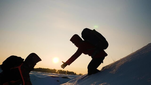 teamwork business. overcome difficulties by giving helping hand fellow partner. two people with backpacks sunset. climber pulls his comrade hand up snowy mountain. go victory. teamwork win. silhouette