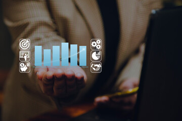 A business person or entrepreneur holds a holographic bar chart with financial and business icons,...