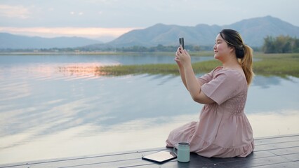 Woman Using Tablet by Lake at Sunset, Surrounded by Majestic Mountains. Digital nomad freelancer,...
