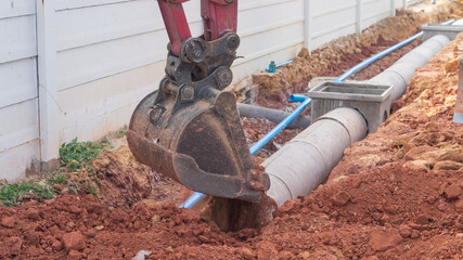 Excavator is digging soil into the drain pipe, construction of a drainage road.