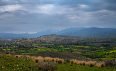 Breathtaking landscape of rolling hills and lush greenery under a moody sky at sunset