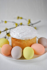 A beautifully decorated easter cake with white icing and sparkly pink sprinkles stands proudly on a plate, surrounded by pastel-colored eggs in shades of yellow, pink, peach, and lavender.