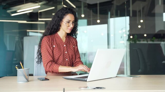 Happy businesswoman working on laptop computer sitting at workplace in a modern business office. Smiling female employee satisfied with completed task, successful transaction or great news read online