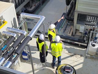 Three engineers in safety vests and hard hats are inspecting an industrial cooling system on a...