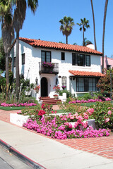 Fototapeta premium Spanish-style home with a red tile roof and vibrant pink flower gardens under a clear blue sky.