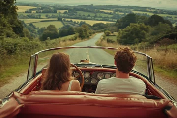 Couple driving classic convertible car on country road through green hills