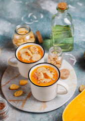 Roasted butternut squash soup with cream and pumpkin seeds on two white mugs.