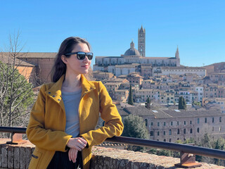 Naklejka premium A portrait of a young woman at the background Siena historical city center panorama. Self tourism concept. Travel in Italy in winter