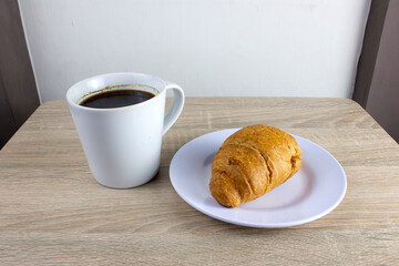 Croissant bread and a cup of coffee on a wooden table