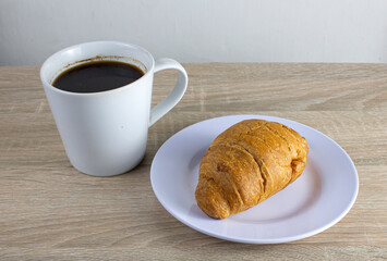 Croissant bread and a cup of coffee on a wooden table