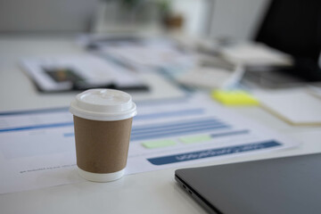 A desk with a laptop, a calculator, a plant, and a stack of papers. The desk is cluttered with...