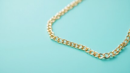 A delicate gold necklace laid out on a pastel teal surface.