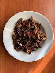 Dried mushrooms on a white ceramic plate placed on a wooden table in natural lighting