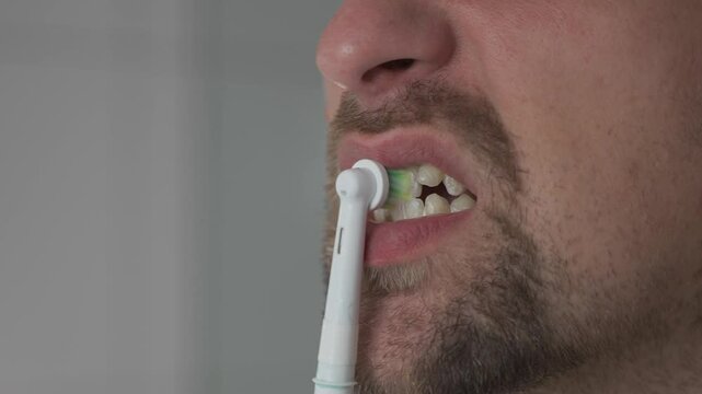 Close-up of man cleaning teeth by an ultrasonic toothbrush. Male brushing his teeth with electric teethbrush. Theme oral health and dental hygiene. Morning sanitation procedures in the bathroom. 