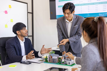 A group of people are sitting around a table with a model house in the middle. They are all smiling and seem to be enjoying themselves

