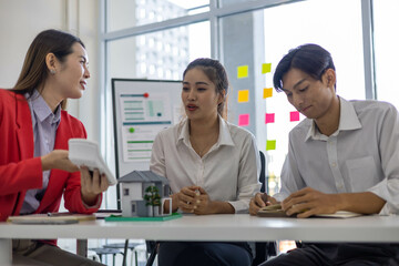 Three people are sitting at a table in a room with a whiteboard behind them. They are discussing something important
