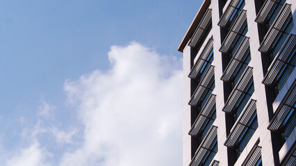 a modern building facade with angular window shades, set against a bright blue sky with scattered...