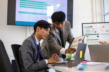 Two men in suits are looking at a computer screen with graphs and charts. They are discussing the data and making decisions based on the information presented. The atmosphere is serious and focused
