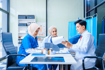 In a hospital setting, an Asian middle-aged man, a middle-aged Muslim woman in hijab, and a middle-aged Asian woman, all medical doctors, collaborate with a nurse to provide expert patient care.