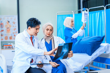 In a hospital setting, an Asian middle-aged man, a middle-aged Muslim woman in hijab, and a middle-aged Asian woman, all medical doctors, collaborate with a nurse to provide expert patient care.