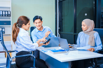 Obraz premium Middle-aged Asian man and Muslim woman in hijab sit across from each other in business meeting. They review report documents, discussing strategies and making decisions, successful, professional.