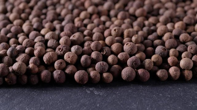 allspice or Jamaican pepper on a black stone table, close up.