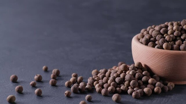 allspice or Jamaican pepper in a wooden bowl on a black stone table.