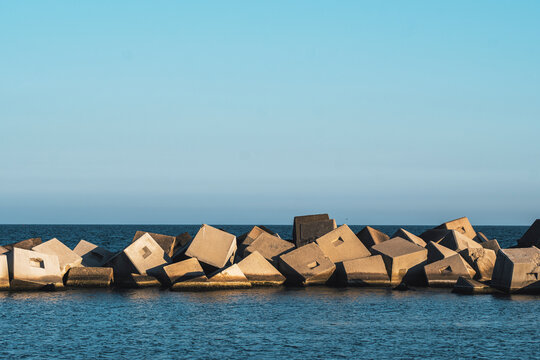 Breakwater blocks forming a structured coastal barrier against the waves. The repetitive concrete elements create a strong geometric pattern along the shoreline.
