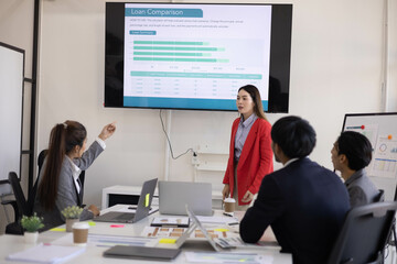 A group of people are working together in a conference room. They are all smiling and seem to be enjoying their time. There are several laptops and papers on the table, and a TV is mounted on the wall