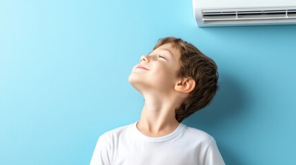 Happy boy enjoying cool air from an air conditioner while standing against a blue wall, feeling relaxed and content in warm weather