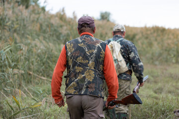 Mature hunter man holding a shotgun and walking through a field