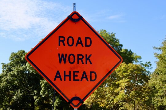 A close view of the orange road work ahead sign.