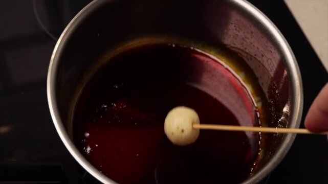 Dipping coconut balls of Brazilian dessert bala baiana in sugar syrup. Traditional caramelized coconut treat preparation.
