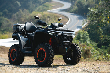 A sleek black ATV parked by a winding road, surrounded by lush greenery, showcasing its rugged design and off-road capabilities.