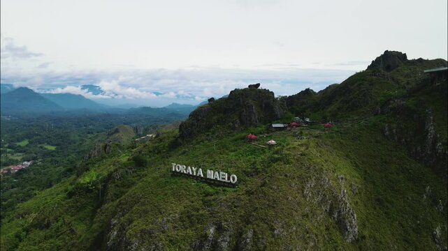 aerial footage of the landmark &ldquo;toraya maleo&rdquo; on a hill with green landscape and clouds