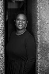 A confident woman stands between two textured walls, looking directly at the camera with a poised...