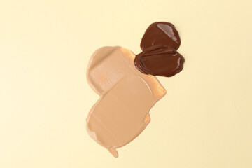Samples of different foundations on beige background, above view
