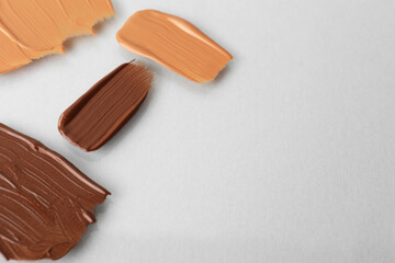 Samples of different foundations on light grey background, closeup. Space for text