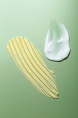 Cream samples on green background, top view
