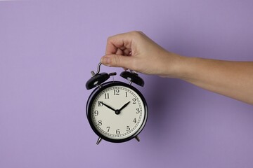 Woman with alarm clock on lilac background, closeup