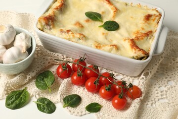 Delicious spinach lasagna in baking dish and ingredients on white table