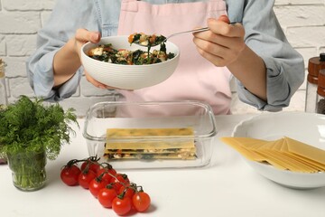 Woman making spinach lasagna at white table indoors, closeup