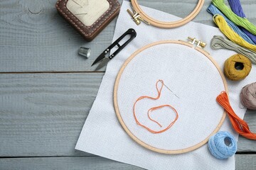 Different sewing supplies for embroidery on grey wooden table, flat lay. Space for text