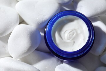 Jar of nourishing cream on white pebble stones, top view